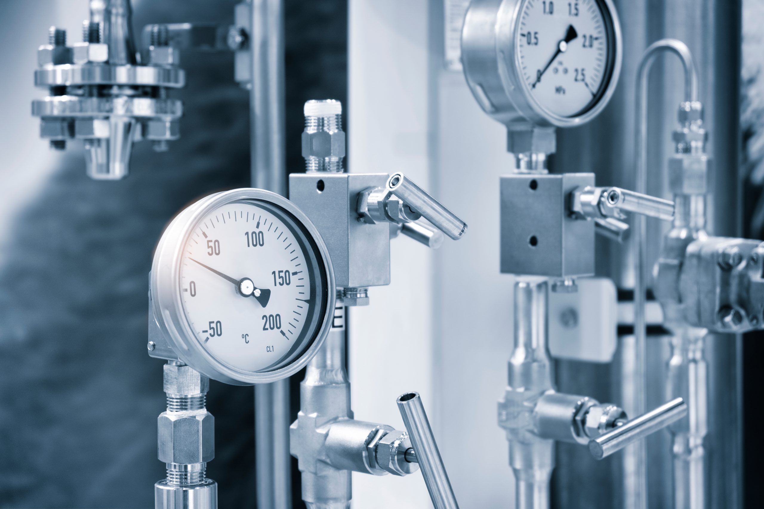 Pressure gauge mounted on stainless steel industrial piping within a mechanical processing system.