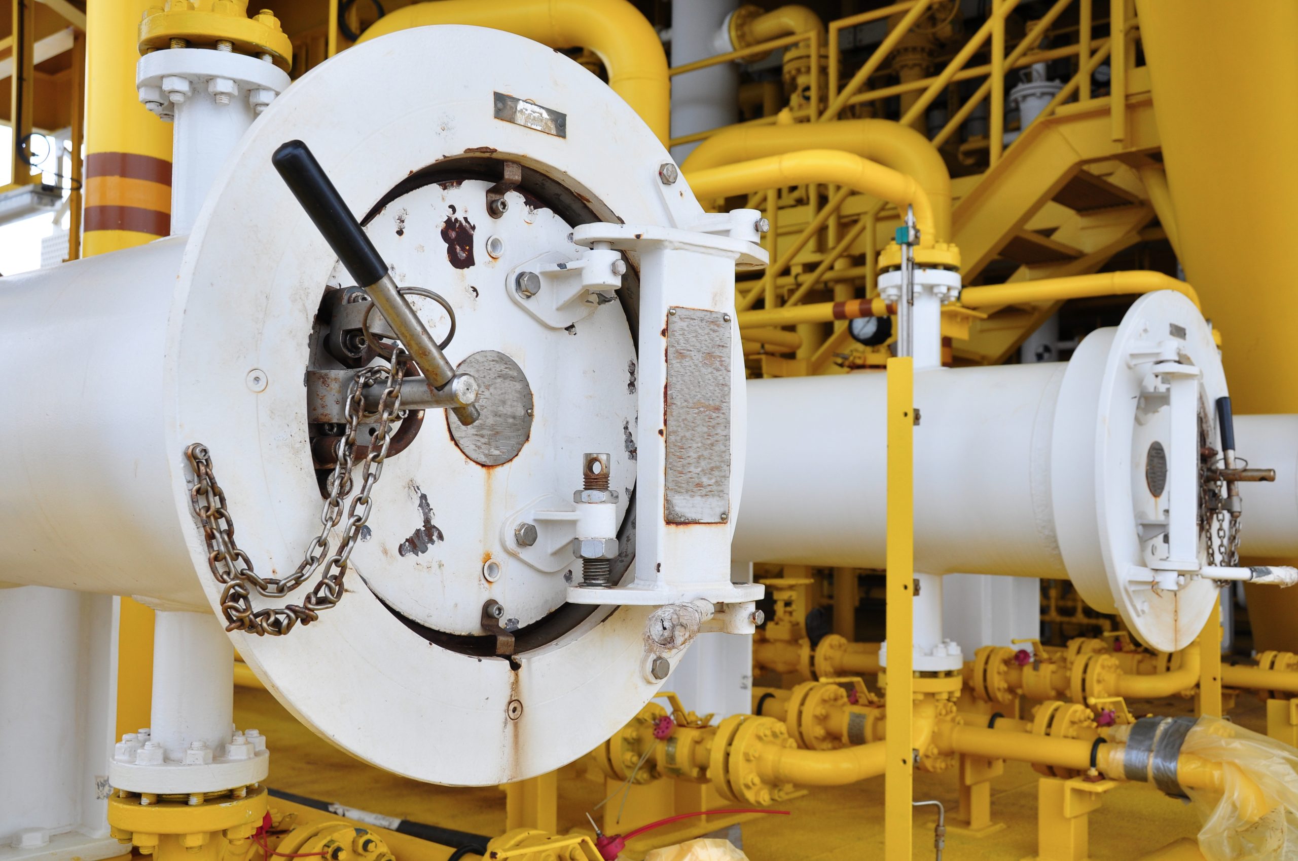 Large industrial pipeline access vessel with bolted closure door and safety chains installed in a yellow processing facility.