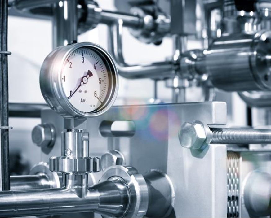Pressure gauge mounted on stainless steel industrial piping within a mechanical processing system.